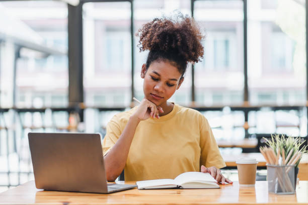istock Young African American woman is taking notes in a notebook while watching a webinar video course. Afro american student listening to the lecture to study online through e-learning. 1589570231