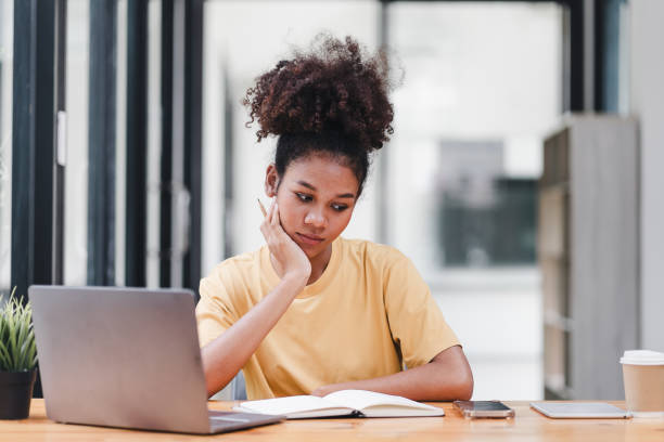 istock Young African American woman is taking notes in a notebook while watching a webinar video course. Afro american student listening to the lecture to study online through e-learning. 1589570256