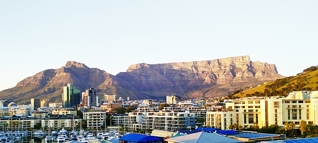 Cape Town's iconic landmark, Table Mountain, rises behind the buildings of the expensive Waterfront complex and the downtown central business district. The tall buildings that can be seen are mostly built on reclaimed land known as the Foreshore, and tend to house financial institutions, law firms and headquarters of other professional firms. This image was shot from a high vantage point in the V&A Waterfront just after dawn.