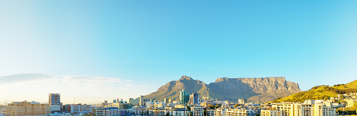 Cape Town's iconic landmark, Table Mountain, rises behind the buildings of the expensive Waterfront complex and the downtown central business district. The tall buildings that can be seen are mostly built on reclaimed land known as the Foreshore, and tend to house financial institutions, law firms and headquarters of other professional firms. This image was shot from a high vantage point in the V&A Waterfront just after dawn.