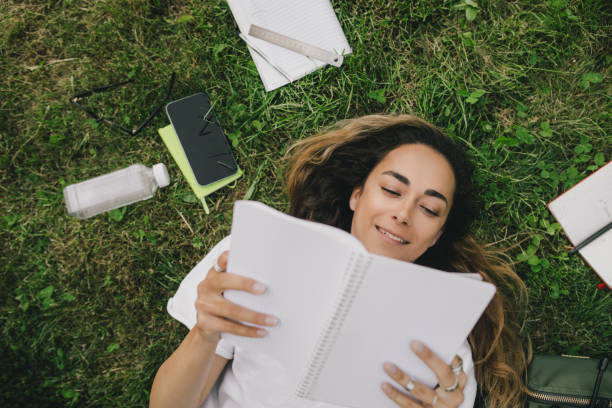 istock Young woman student studying using her books, laptop and notebook, sitting on grass. 1589602481