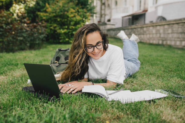 istock Young woman student studying using her books, laptop and notebook, sitting on grass. 1589602488