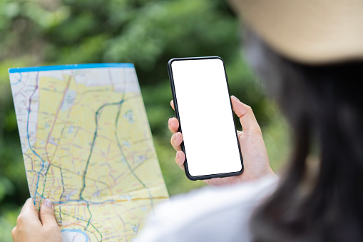 Close up of woman hands with a smartphone and map in the forest, soft focus background, isolate screen.
