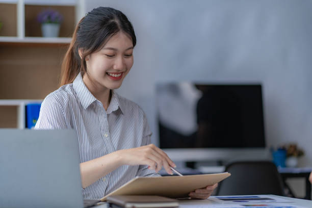 istock Young Asian accountant working on her project budget calculator Working in office with laptop computer doing tax document check balance calculation report 1589607258