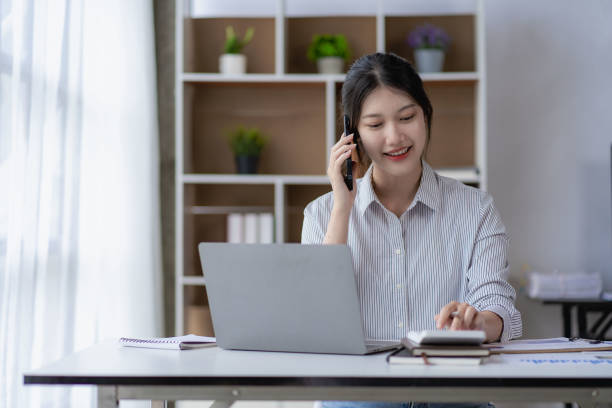 istock Young Asian accountant working on her project budget calculator Working in office with laptop computer doing tax document check balance calculation report 1589607261