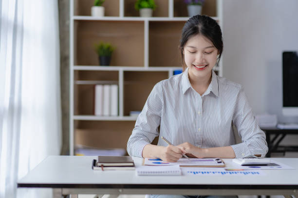 istock Young Asian accountant working on her project budget calculator Working in office with laptop computer doing tax document check balance calculation report 1589607264