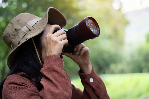 Asian female tourist backpacking in hat taking pictures with camera and going for a tropical forest. Walk summer nature. Holiday travel concept