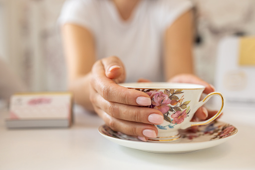 A mid adult Caucasian woman holding a decorative tea cup in a nail salon with her nails done