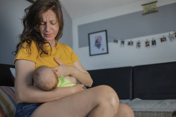 Young mother is breastfeeding her newborn baby boy and she is feeling the pain. stock photo