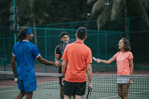 Asian mixed doubles Tennis players greeting touching tennis racket over tennis net with opponent before game begin