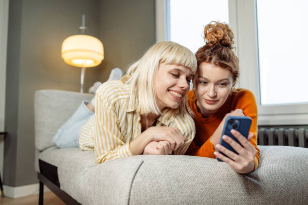 istock Two young female friends lying on a sofa and looking at a phone 1589623562