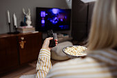 A young Caucasian woman holding popcorn and switching TV channels