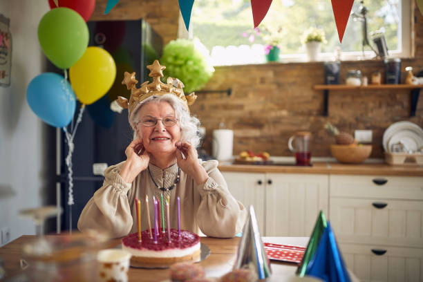 Radosna, szczęśliwa, urocza starsza kobieta w dmuchanej koronie, świętująca urodziny samotnie w domu, czująca się szczęśliwa. – zdjęcie