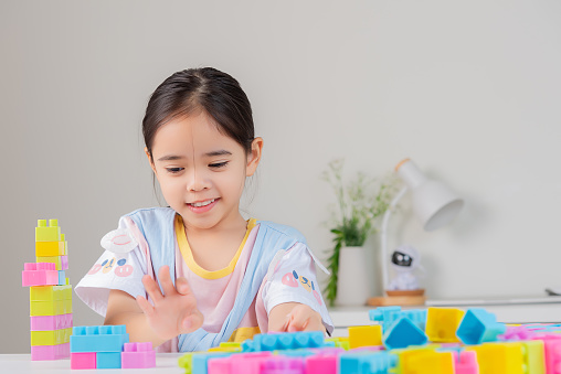 little girl wearing a bright shirt is happy Playing colorful block puzzles. in the white room