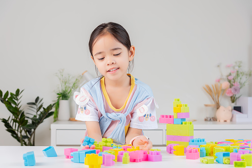 little girl wearing a bright shirt is happy Playing colorful block puzzles. in the white room