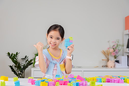 little girl wearing a bright shirt is happy Playing colorful block puzzles. in the white room