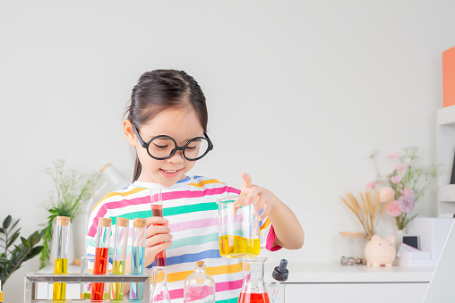 Asian little girl Wear a brightly colored shirt and glasses working with test tube science experiment in white classroom