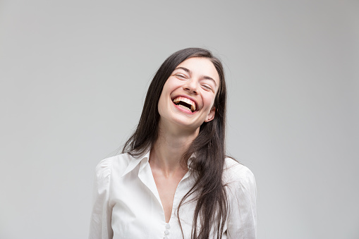 Frontal central portrait of a happy woman, positively struck, who laughs and smiles with immense joy. Wearing a formal white shirt, long hair, great teeth, filled with good news and positivity