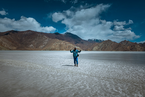 With Pangong Lake's icy surface as a backdrop, an Indian adult showcases pure happiness and a sense of adventure during their remarkable visit in late March 2023.