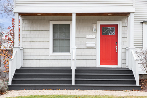 Detail of a home's front porch and red front door.