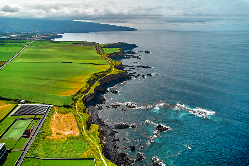 Aerial shot, drone point of view, picturesque nature of Azores. Green hills and cloudy sky, Atlantic Ocean view during sunny summer day. Sao Miguel, Ponta Delgada island. Portugal