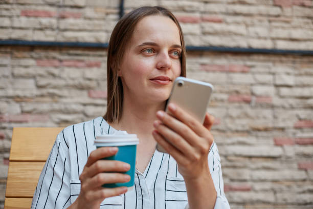 istock Concentrated brown haired businesswoman in formal attire while using smartphones drinking coffee in cafe recording voice message. 1589866836