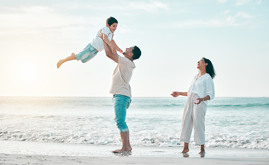 Family, beach and father lifting boy child with love, freedom and travel celebration in nature. Flying, fun and parents with kid at the ocean for bond, happy and airplane game while traveling in Bali