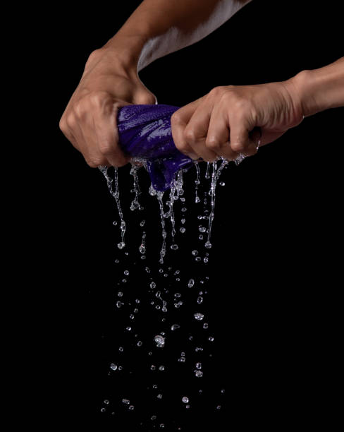 Two hands wring wet cloth after washing by twist and squeeze over dark background
