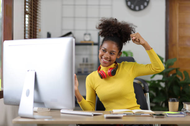 istock Beautiful african woman showing joyful expression while looking at computer screen. 1589889666
