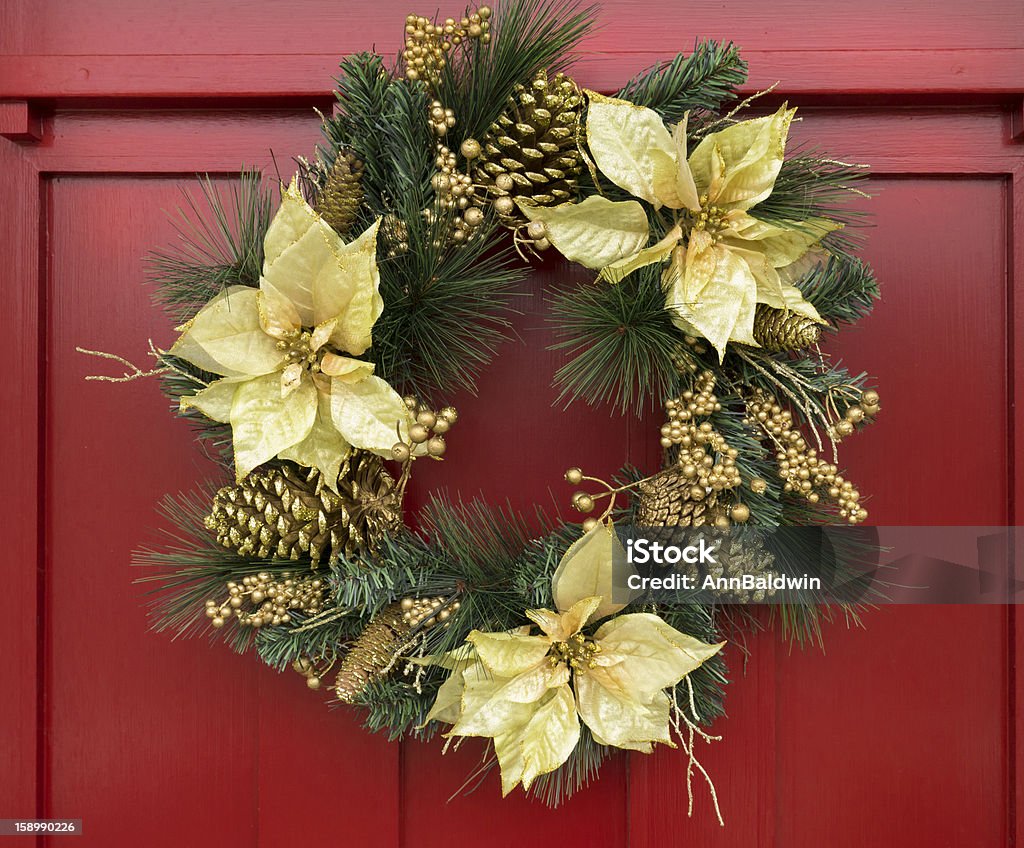 Christmas wreath on red painted door Ornate holiday wreath with gold silk poinsettia, painted gold cones, and berries among pine leaves hanging on red-painted door. Gold Colored Stock Photo