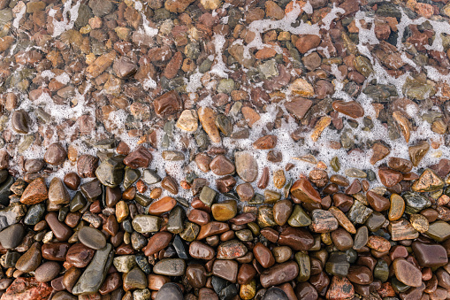 An overhead shot of a pebbly shoreline in Torridon, Scotland. The water is covering half of the stones and there are bubbles on the surface.