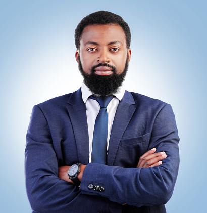 Serious, crossed arms and portrait of businessman in a studio with success, confidence and leadership. Pride, professional and headshot of a young, male and African lawyer isolated by blue background