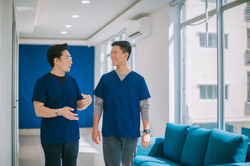 2 chinese male nurses walking in corridor talking in hospital during coffee break