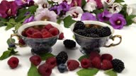 istock Raspberries and blackberries fall into cups with berries against the background of mallow flowers, slow motion 1589934874