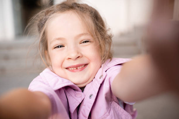 Cute kid girl 4-5 year old making selfie or taking video on phone. Looking at camera. Childhood.