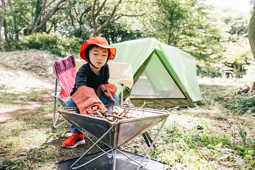 Japanese boy mixing the camping firepit at campground. Waiting for the family to start cooking in nature.