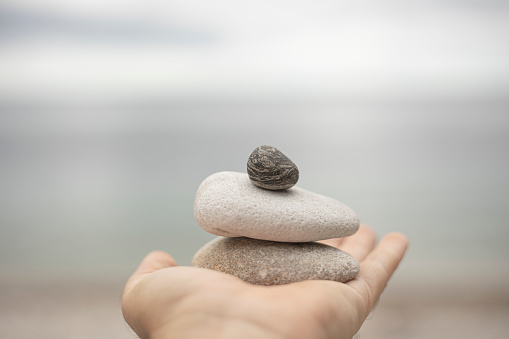 Hand with stack of pebbles on the beach on a bright and calm day