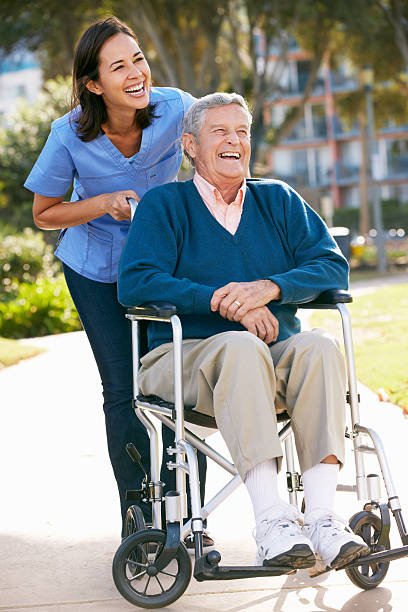 senior hombre empujando carer para silla de ruedas - care community 80 plus years cheerful fotografías e imágenes de stock