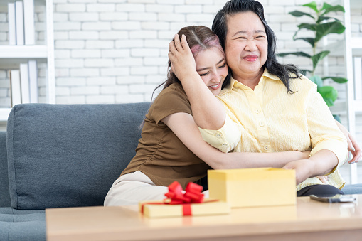 Asian cute daughter hugged mother after giving present surprise birthday box with gift or present box , red ribbon that opened in foreground.