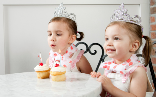 Little Girls blow out birthday candles on cup cakes.