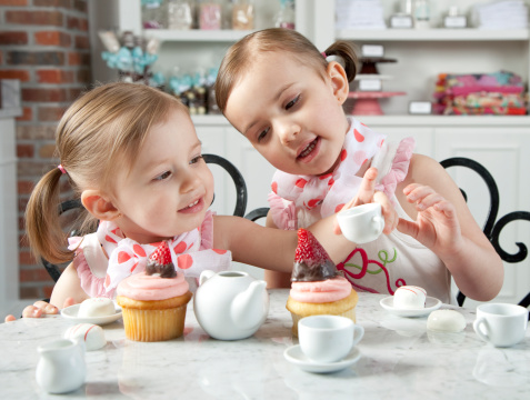 Two little Girls play tea with candy in the background