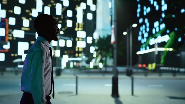 African american person on night walk downtown under streetlights, admiring modern office buildings from illuminated sidewalk. Confident man enjoying nighttime promenade around town.