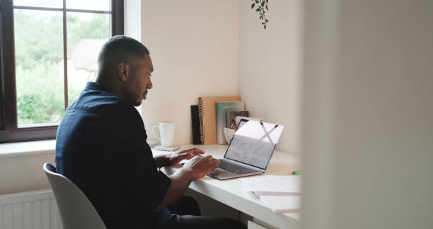 istock Remote work, laptop and black man in home office typing email, internet search or networking online. Technology, communication and freelancer with computer at desk in apartment on research project. 1589979857