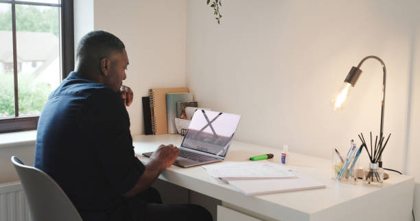 istock Remote work, laptop and black man in home office for research project, internet search or networking online. Technology, communication and freelancer with computer at desk in apartment typing email. 1589979869
