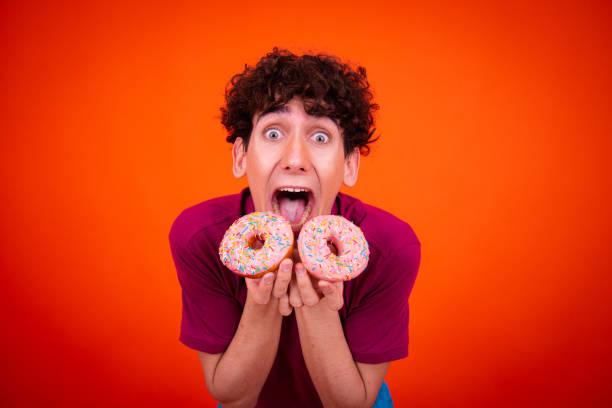 istock Young attractive guy eats pink donuts. Delicious breakfast and good vibes. 1589996407