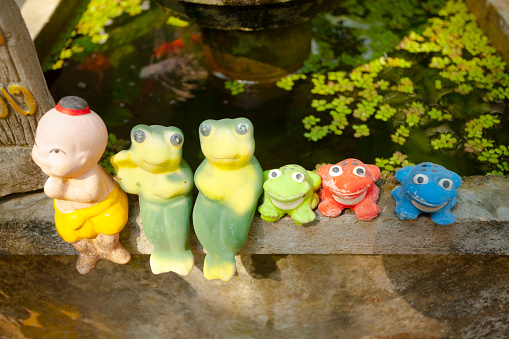 Group of colored thai figurines decor outside of house in On Tai, Chiang Mai, San Kamphaeng district of Chiang Mai, which is cultural heritage and art and craft center in north Thailand. In a row are a human fugurine and frogs at a small basin.