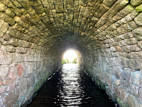Inside an old stone lined tunnel with a stream flowing through