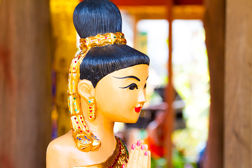 Headshot of wooden female thai statue with Wai gesture welcoming people at cultural old house in On Tai, Chiang Mai, San Kamphaeng district of Chiang Mai