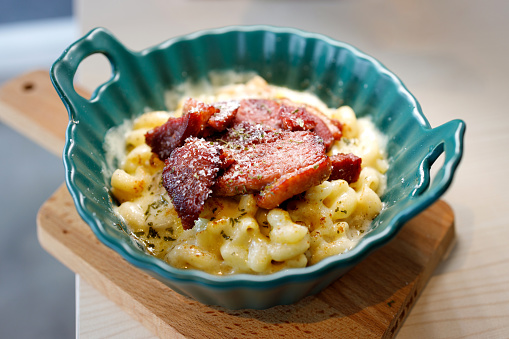 On a ceramic plate, there is a serving of delicious baked macaroni with cheese and smoked duck meat