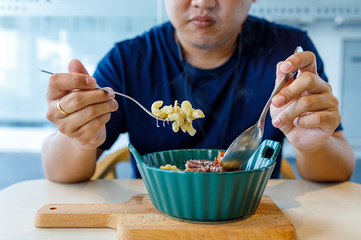 A cropped shot of an Asian man savoring delicious baked macaroni with cheese and smoked duck meat in a restaurant